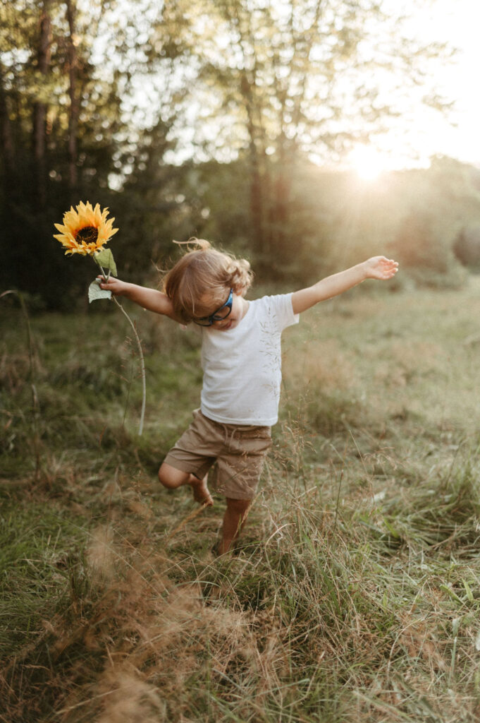 Image is of Darian holding a sunflower in a grassy field.