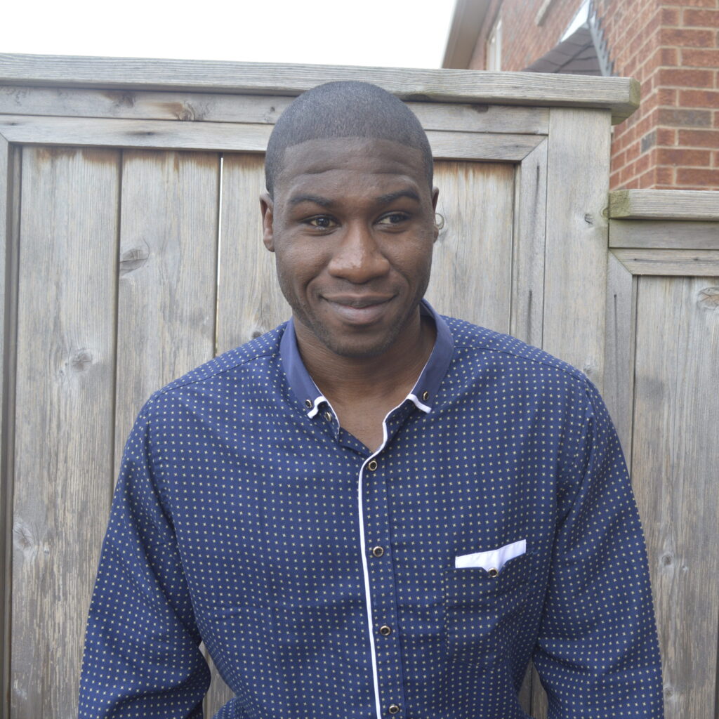 Photo of Ben Akuoko. Ben is smiling and is wearing a dark blue-patterned button-down shirt.