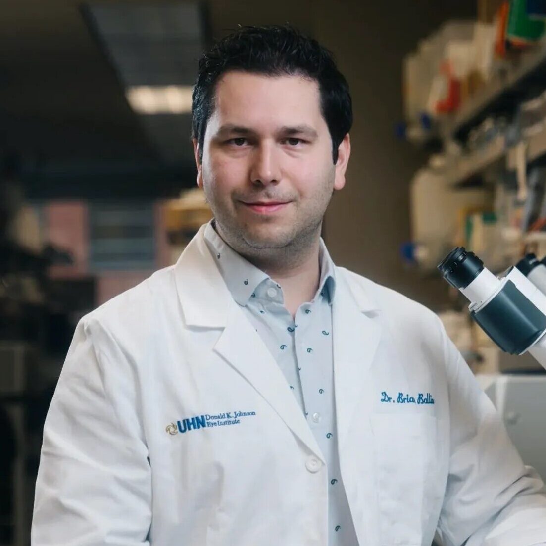 Photo of Dr. Brian Ballios. Dr. Ballios is in a white lab coat inside his laboratory and is looking at the camera.