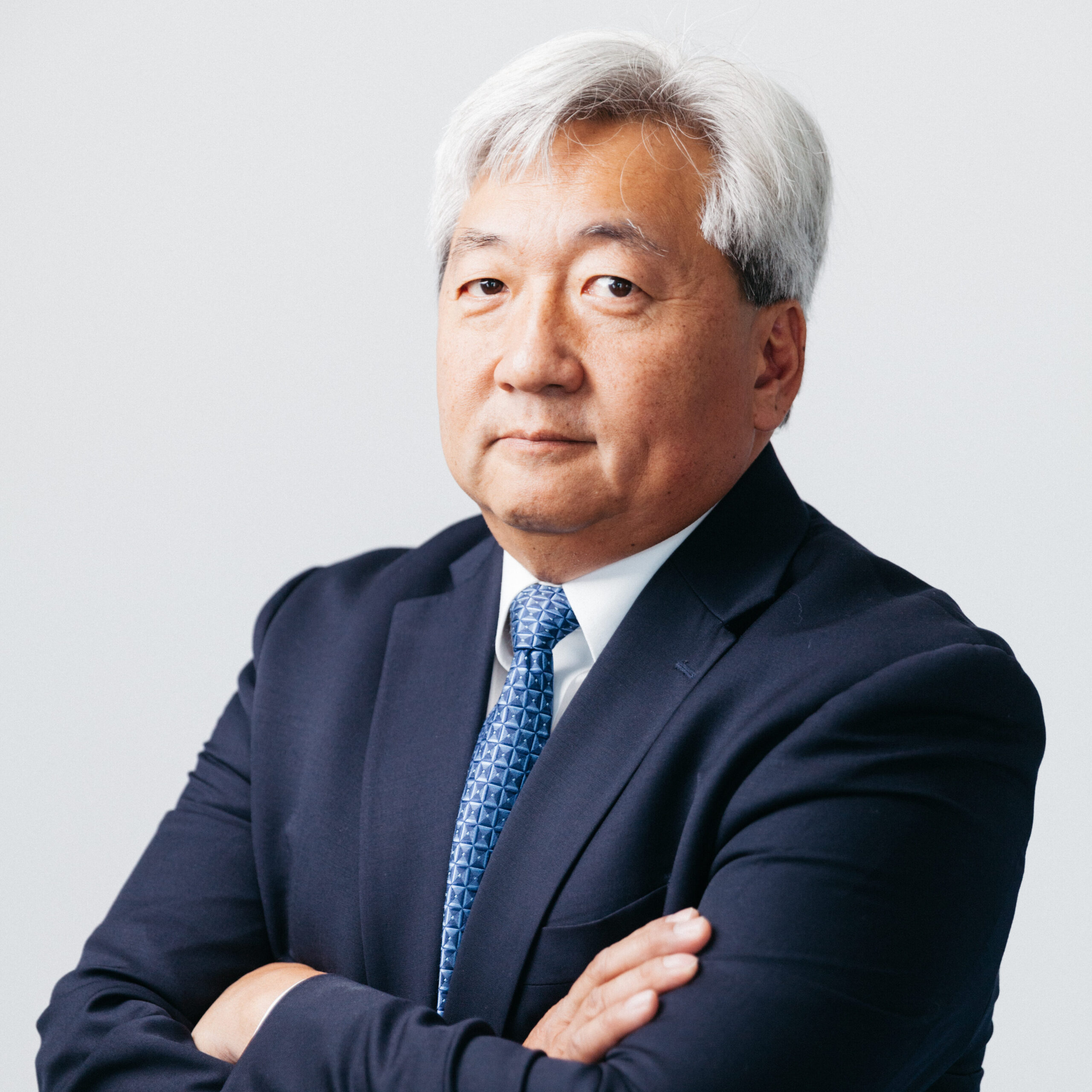 Photo of Dr. Daniel Chung. Dr. Chung is wearing a navy blue suit, light blue tie and white shirt and is looking at the camera with his arms crossed.