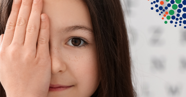 Girl covering one eye with eye chart behind her and FBC iris in the background.