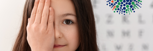 Girl covering one eye with eye chart behind her and FBC iris in the background.